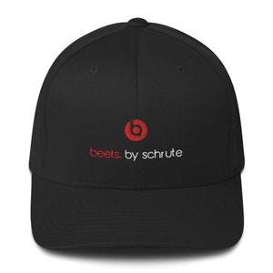 Puede incluir: Gorra de béisbol negra con visera curva. La gorra presenta el texto "beets. by schrute" en rojo y blanco, con un logotipo rojo encima. La gorra está hecha de un material suave.