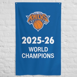 May include: A rectangular blue wall banner featuring the New York Knicks logo at the top, which includes an orange basketball and the team name in orange and grey. Below the logo, the text reads 2025-26 WORLD CHAMPIONS in bold white letters.