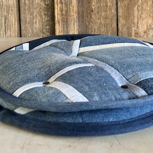 Könnte beinhalten: Ein rundes Denim-Kissen mit Patchwork-Design. Das Kissen besteht aus verschiedenen Blautönen von Denim und hat einen weißen Besatz. Das Kissen hat einen Durchmesser von etwa 40 cm.
