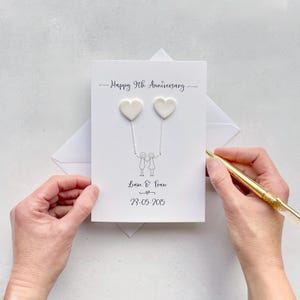 May include: A white anniversary card with the text "Happy 9th Anniversary". Two white heart-shaped decorations are connected to a stick figure couple. The names "Liam & Fran" and the date "23-05-2015" are also printed on the card.