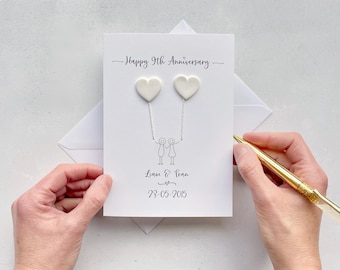 Könnte beinhalten: Eine weiße Jubiläumskarte mit dem Text "Happy 9th Anniversary". Zwei weiße herzförmige Dekorationen sind mit einem Strichfigurenpaar verbunden. Die Namen "Liam & Fran" und das Datum "23-05-2015" sind ebenfalls aufgedruckt.