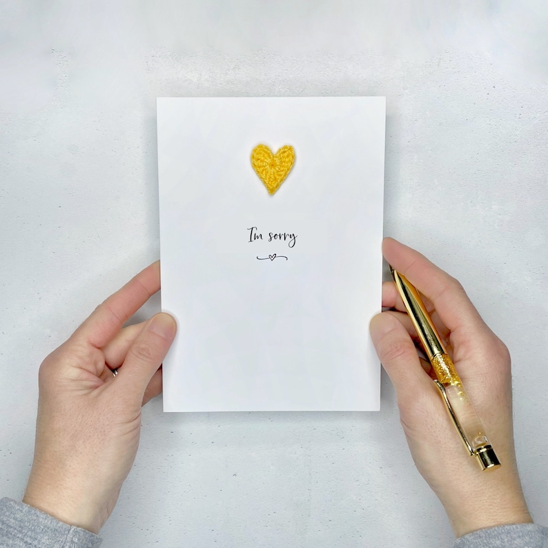 A white (portrait) card with I’m sorry printed in the centre in black cursive text. Under this, a little black squiggle line and black heart has been printed. A mini cotton yellow crochet heart has been stuck above the words I’m sorry.