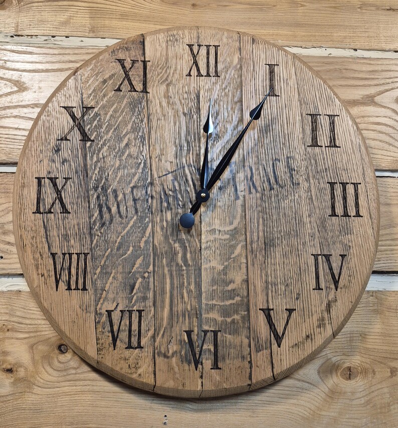 May include: A round wooden clock with Roman numerals. The clock face is made of light brown wood with dark brown markings. The clock hands are black. The clock is mounted on a wooden wall.
