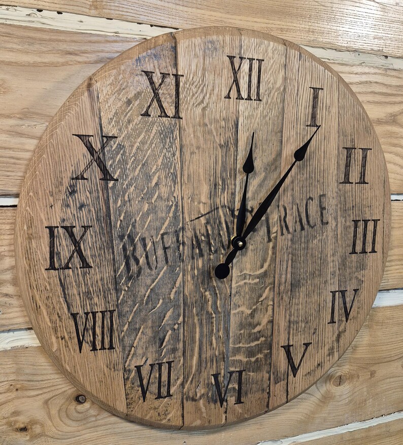 May include: A round wooden clock with Roman numerals and black hands. The clock face is made of light brown wood with visible grain and the text "BUFFALO TRACE" is partially visible. The clock is mounted on a wooden wall.
