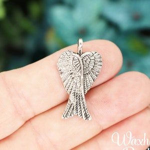 May include: Silver angel wing charm with a detailed design. The wings are shaped like a heart and have a textured finish.