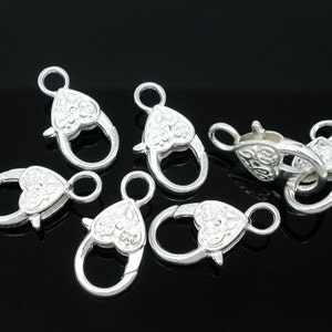 May include: Six silver-toned heart-shaped clasps with intricate designs. These clasps are perfect for adding a touch of elegance to jewelry making projects.