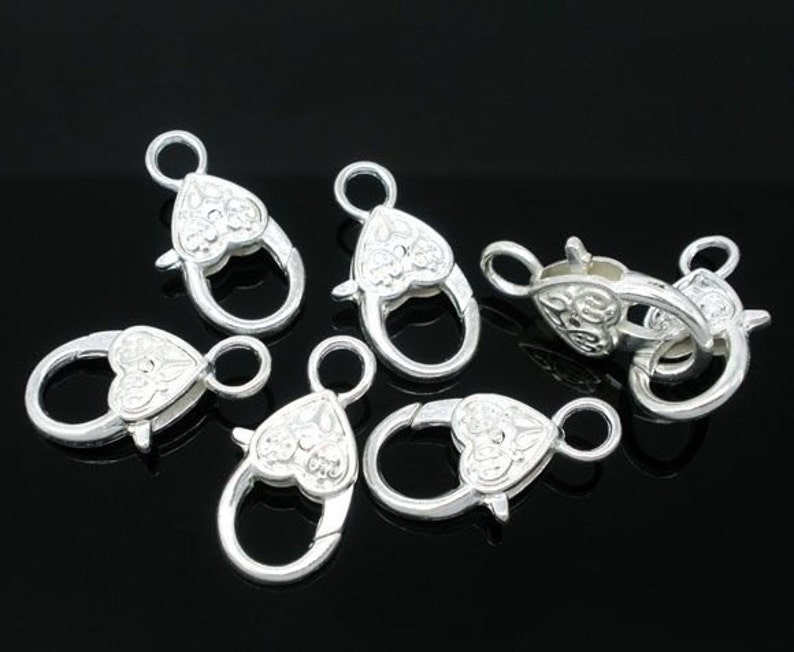 May include: Six silver-toned heart-shaped clasps with intricate designs. These clasps are perfect for adding a touch of elegance to jewelry making projects.