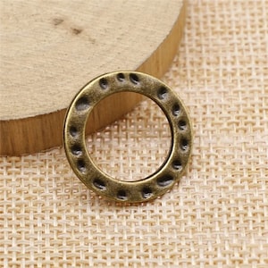 May include: A bronze-colored metal ring with a textured surface. The ring is round and has a hole in the center.