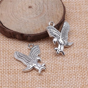 May include: Two silver eagle charms with detailed wings and a textured finish. The charms have a loop at the top for attaching to jewelry or other crafts.
