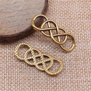 May include: Two gold-toned metal charms in the shape of an infinity knot. The charms are intricately designed with a textured surface.