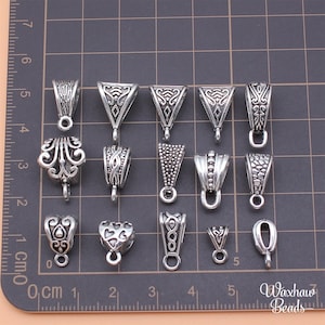 May include: Assortment of 12 silver-toned metal pendant bails with various ornate designs. The bails are arranged in three rows of four on a grid background.