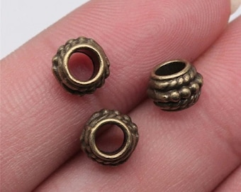 May include: Three small, antique brass-colored beads. Each bead has a central hole and a decorative, textured surface. The beads are likely used for jewelry making or other craft projects.