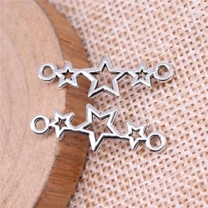 May include: Two silver-toned metal charms featuring a row of five star shapes. Each charm has a loop at either end for attaching to jewelry or other crafts.