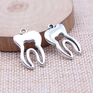 May include: Two silver-toned tooth charms, each with a detailed outline of a tooth, perfect for jewelry making or crafting projects.