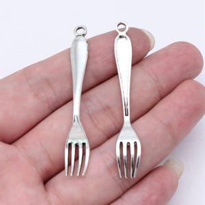 May include: Two silver-toned fork charms with a loop at the top for attaching to jewelry or other crafts.