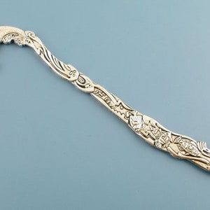 May include: Silver bookmark featuring a dolphin design with intricate details. The bookmark is shaped like a dolphin with its tail curled up. The dolphin is surrounded by a variety of sea creatures, including fish, starfish, and seaweed.