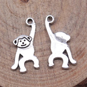 May include: Two silver monkey charms with a loop at the top for attaching to jewelry or other crafts. One monkey is standing with its arms raised, while the other is sitting with its arms down.