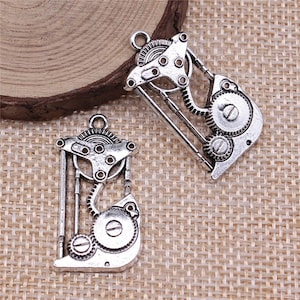 May include: Two silver-toned metal charms shaped like gears and cogs. The charms have a steampunk aesthetic and are perfect for jewelry making or crafting.