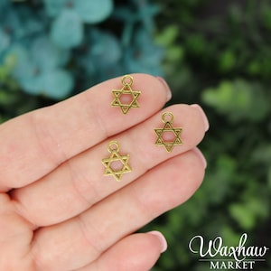 May include: Three gold-colored metal charms in the shape of a Star of David. The charms are small and have a hole at the top for attaching to a necklace or bracelet.