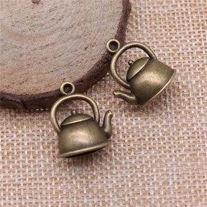 May include: Two antique gold-toned teapot charms. The charms are detailed with a handle, spout, and lid.