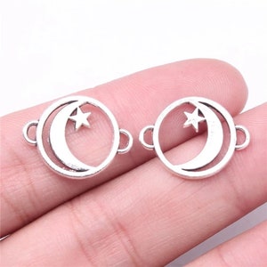 May include: Two silver-toned metal charms in the shape of a circle with a crescent moon and star cutout. The charms have a jump ring on each side for attaching to jewelry.