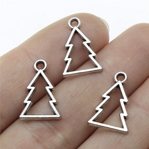 May include: Three silver-colored Christmas tree charms. Each charm is a cutout design of a stylized evergreen tree with a small loop at the top for attaching to jewelry or other crafts. The charms are displayed against a neutral background.