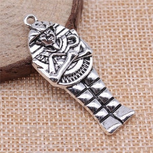 May include: Silver charm pendant featuring an Egyptian pharaoh in a sarcophagus. The charm is detailed with intricate carvings and a textured surface.