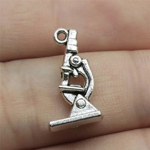 May include: Silver-toned microscope charm pendant. The charm is detailed with a microscope lens and a base.