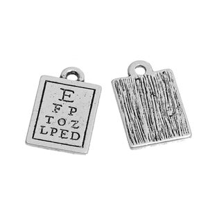 May include: Two silver-toned rectangular charms. One charm features an eye chart with the letters E, F, P, T, O, Z, L, and PED. The other charm has a textured, wood-grain-like pattern. Both charms have a small loop at the top.