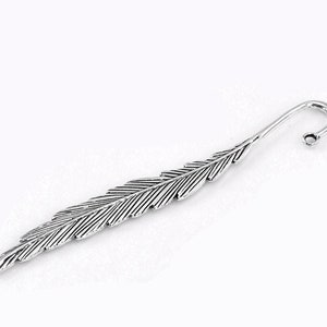May include: Silver feather bookmark with a curled end. The bookmark is detailed with lines to resemble a feather.