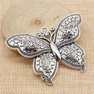 May include: Silver-toned metal butterfly charm with an intricate, ornate design. The charm has a loop at the top for attaching to jewelry or other crafts.