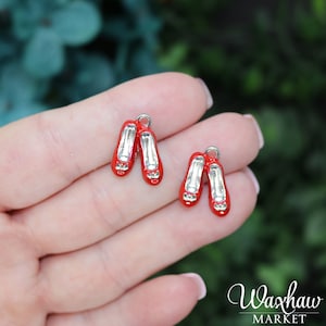 May include: Two red and silver charm pendants shaped like ruby slippers. The charms are about 1 inch long and have a silver loop for attaching to a necklace or bracelet.