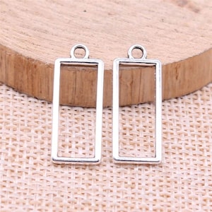 May include: Two silver-toned metal rectangular pendant frames with a loop at the top. The frames are empty and ready to be filled with resin, glass, or other materials.