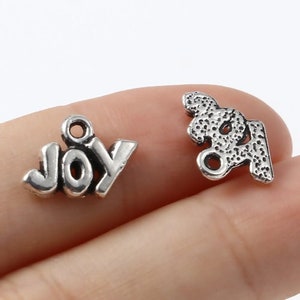 May include: Two silver charms, one with the word "JOY" and the other with a stylized design.