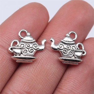 May include: Two silver charm pendants in the shape of a teapot and a teacup. The teapot has a lid and a spout, and the teacup has a handle. Both charms have a swirl design.