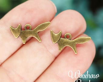 May include: Two antique gold fox charms with a loop for attaching to jewelry or crafts. The charms are on a hand against a green background.