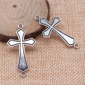 May include: Two silver-toned metal cross charms with a detailed design. Each charm has two jump rings for attaching to jewelry or other crafts.