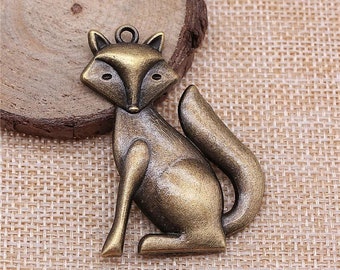 Puede incluir: Un amuleto de metal de color bronce en forma de zorro con un diseño detallado. El zorro está sentado con la cola enroscada alrededor de su cuerpo. El amuleto tiene un bucle en la parte superior para sujetarlo a un collar o pulsera.
