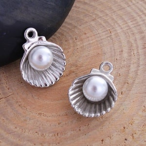 May include: Two silver charm pendants shaped like seashells with a white pearl in the center of each.