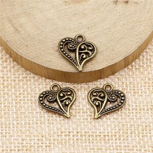 May include: Three antique gold-toned metal heart charms with intricate filigree designs. The charms have a loop at the top for attaching to jewelry or other crafts.