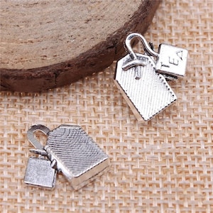 May include: Two silver charm pendants in the shape of tea bags. One charm has the word "TEA" on it.