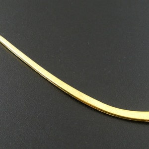 May include: A gold-colored metal bookmark with a curved design. The bookmark is thin and has a smooth surface.