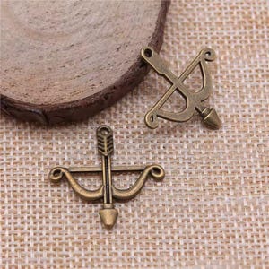 May include: Two antique gold-toned metal bow and arrow charms. The charms are detailed and have a vintage look.