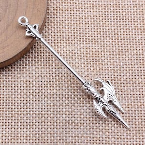 May include: A silver-toned metal spear charm with a detailed design. The spear has a pointed tip and a decorative handle.
