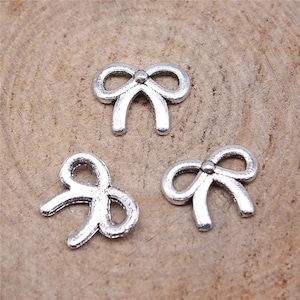 May include: Three silver metal bow charms. The bows are in different styles, with one having a small bead in the center.