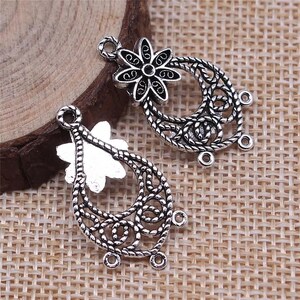 May include: Two silver filigree earring charms with a flower design. Each charm has a loop at the top for attaching to a jewelry piece.