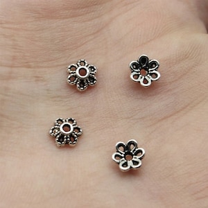 Op de afbeelding: Vier zilverkleurige metalen bloemvormige kralencaps met een klein gaatje in het midden. De kralencaps zijn perfect om een ​​toets van elegantie toe te voegen aan sieradenmaakprojecten.