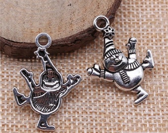 May include: Two silver charm pendants in the shape of a snowman. Both snowmen are wearing hats and scarves and are in a skating pose.