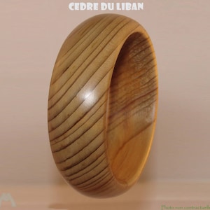Peut inclure: Un bracelet jonc en bois brun clair avec un grain de bois visible. Le bracelet est de forme arrondie et porte l'inscription "CEDRE DU LIBAN" en lettres blanches en haut.