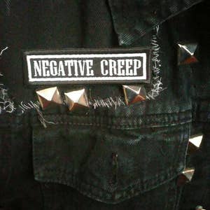 May include: Black denim jacket with a white patch that reads "NEGATIVE CREEP" and silver pyramid-shaped studs.